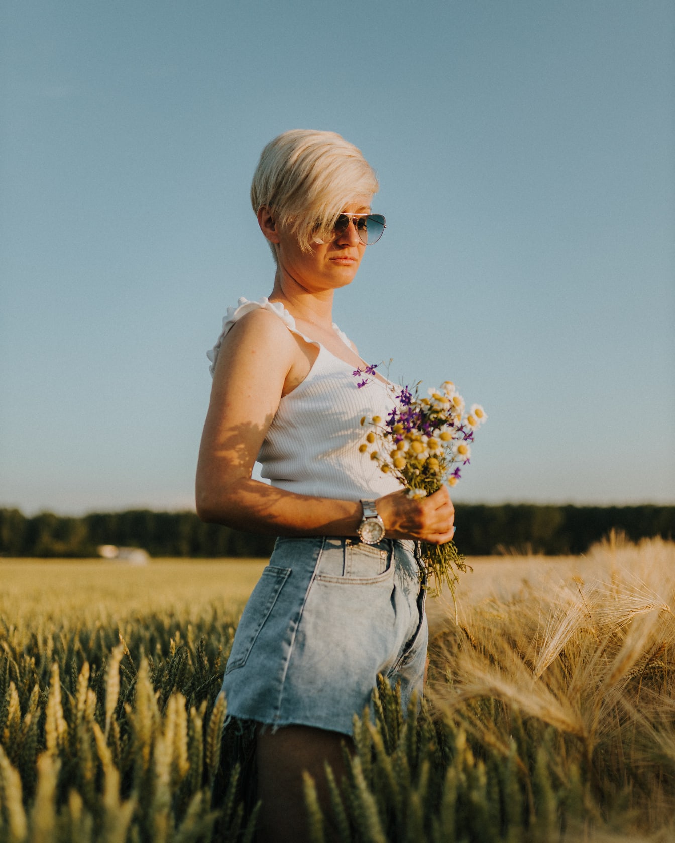 Urocza krótkowłosa blondynka z bukietem kwiatów na polu pszenicy