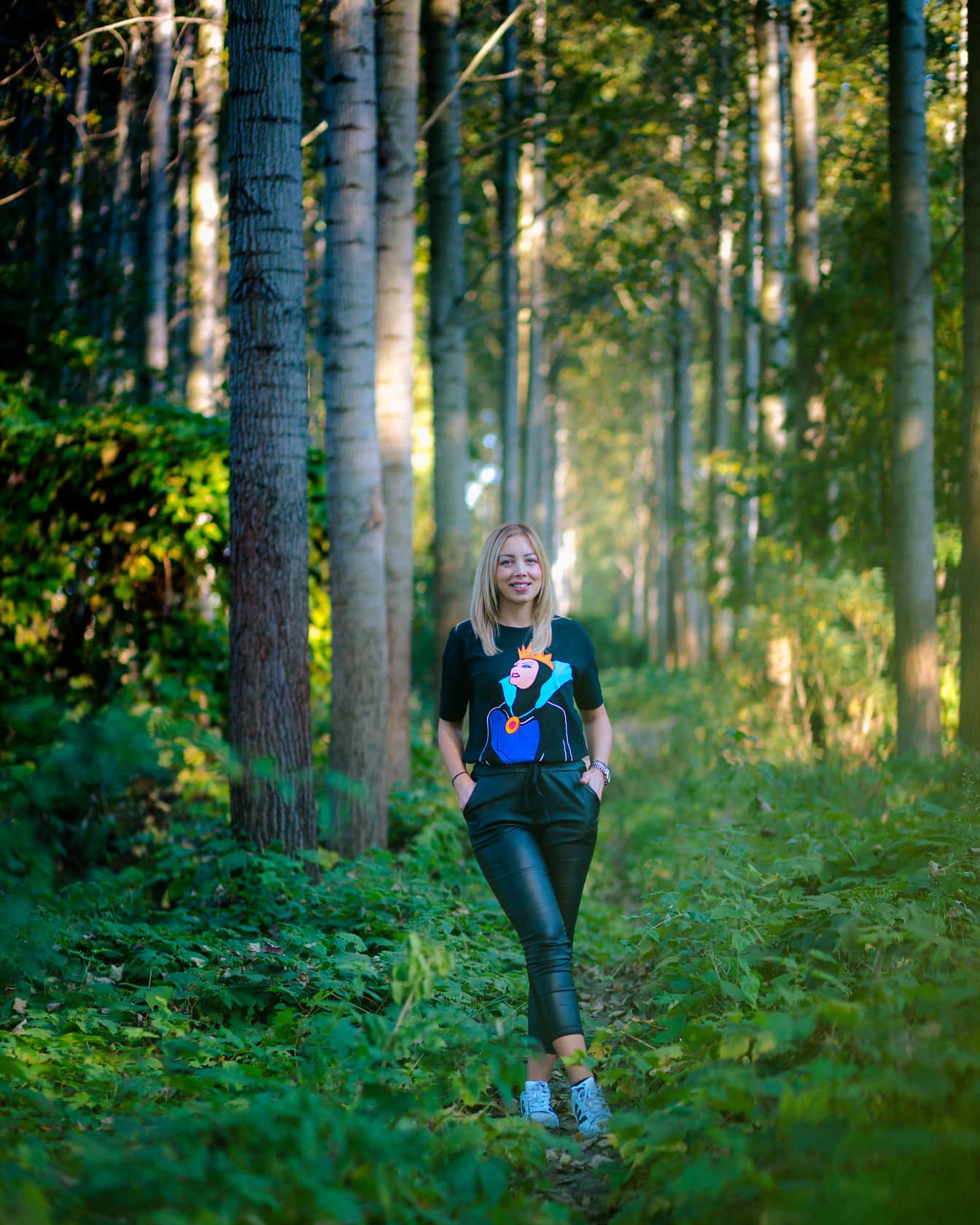 Pekné tínedžerské dievča v čiernych kožených nohaviciach pózuje v lese