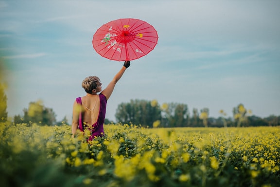 Cheerfully woman in rapeseed with pinkish umbrella