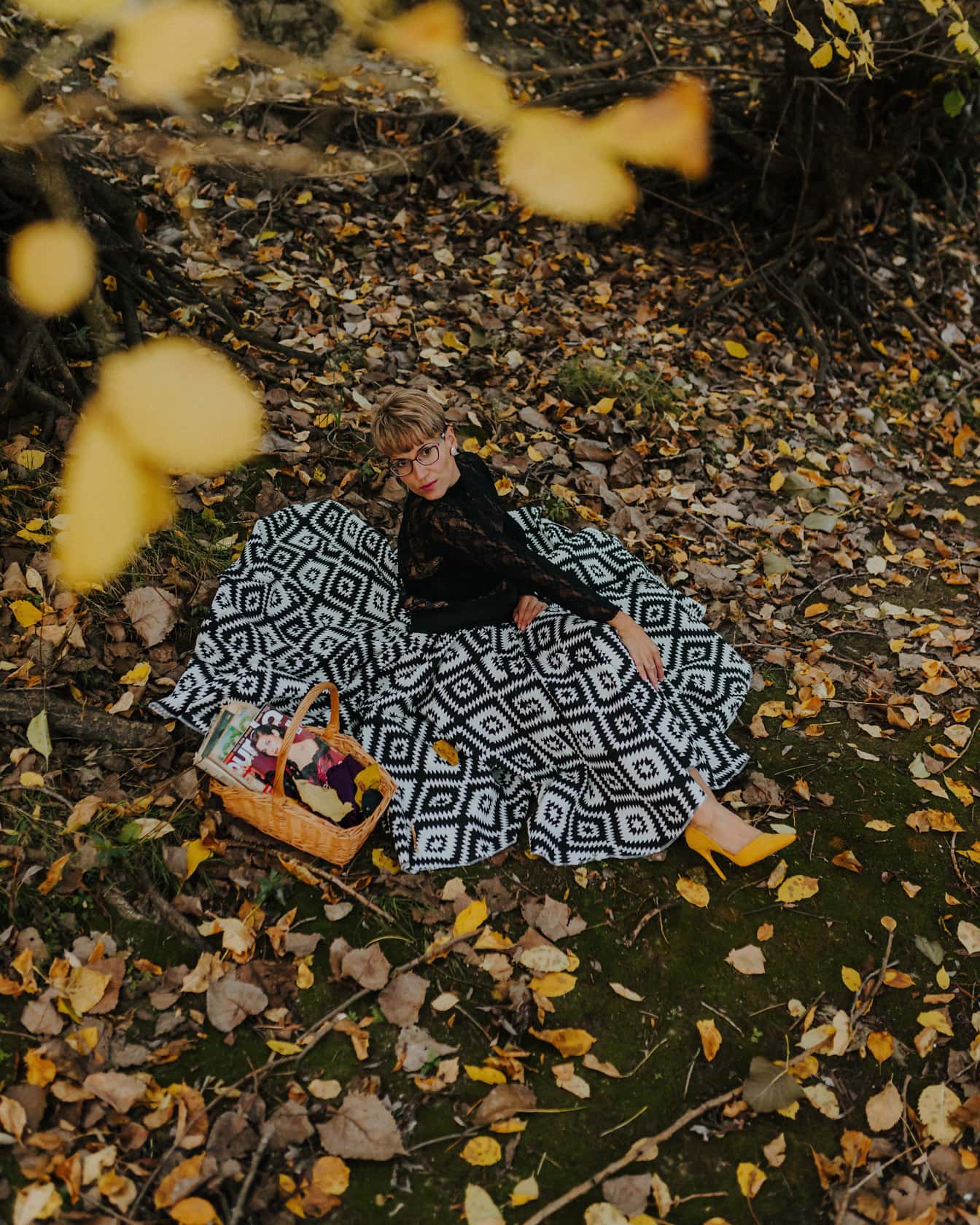 Blondýnka s krátkými vlasy sedí v lese a pózuje v šatech