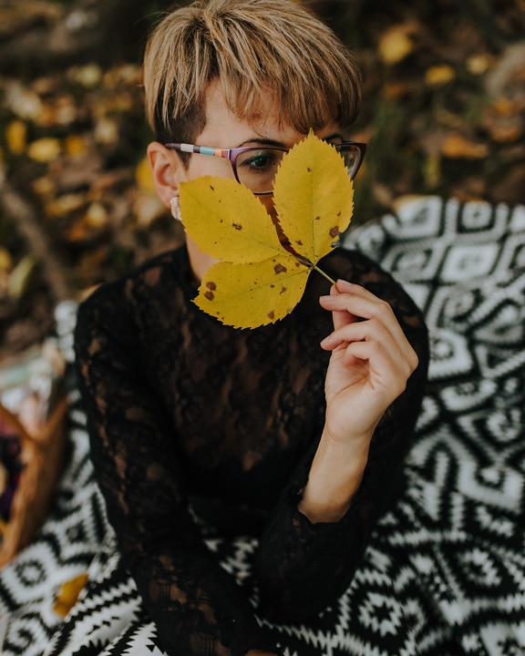 Pretty lady with yellowish autumn leaf on face