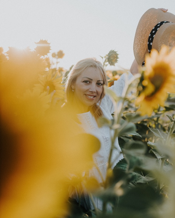 Hübsche fröhliche blonde Haarfrau im Sonnenblumenfeld in der Sommersaison