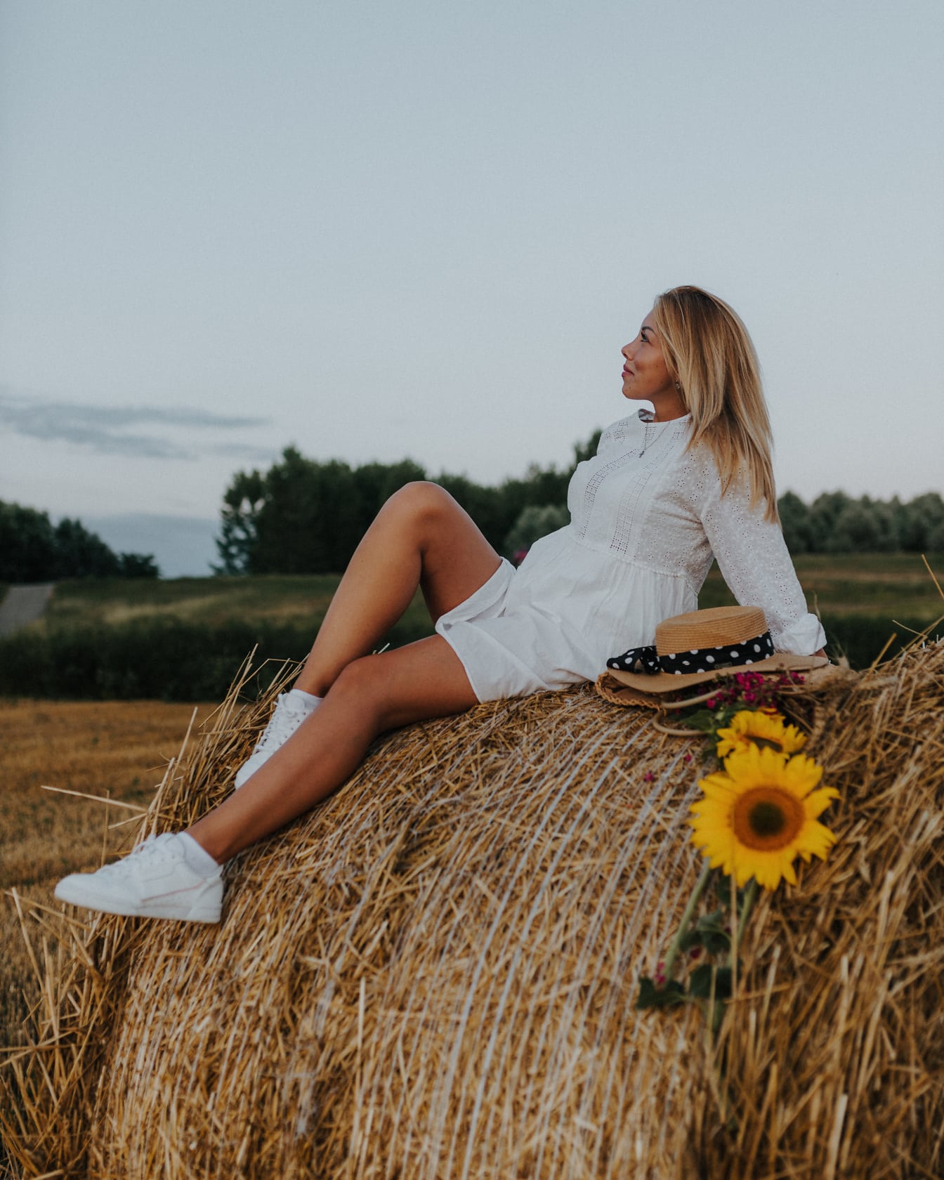 Разкошен блондинки в бял рокля sitting на haystack