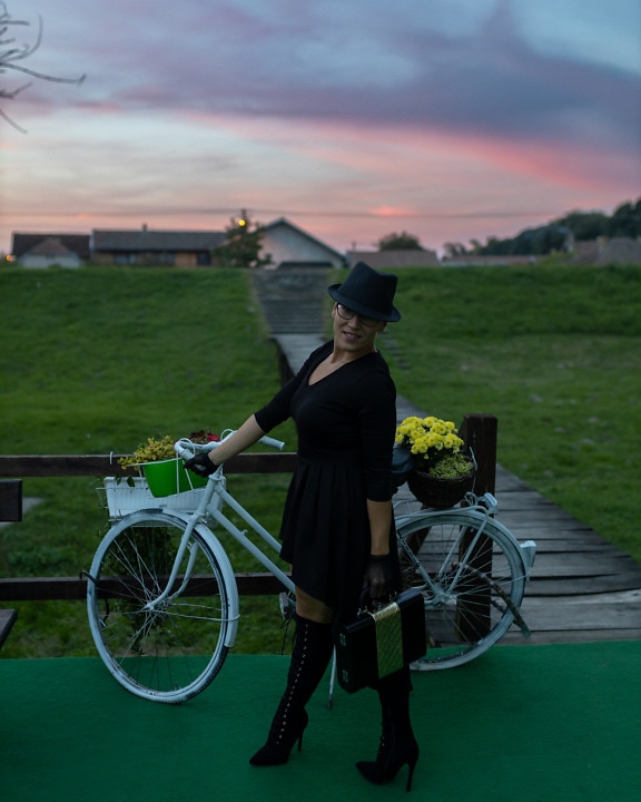 Black elegance woman in black outfit posing with bicycle