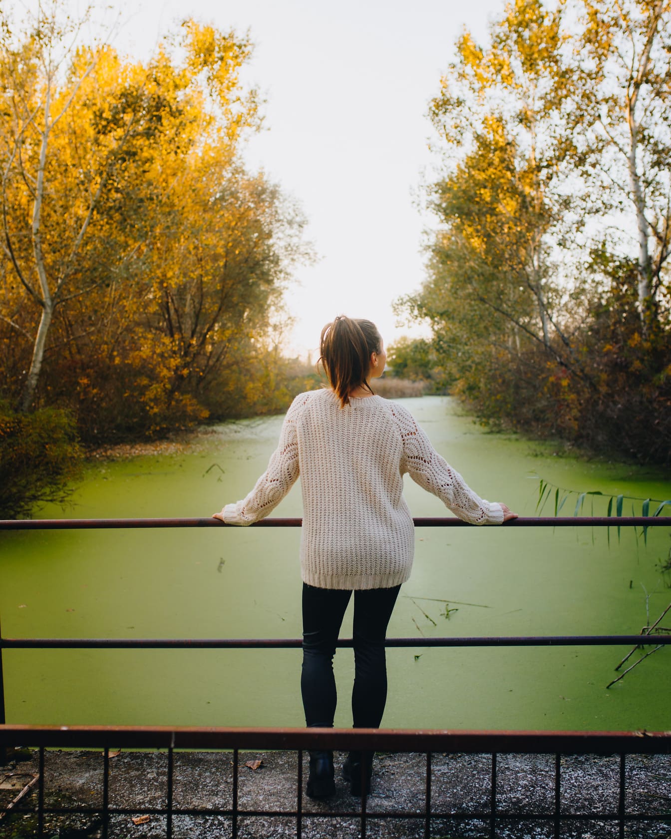 Tânără femeie în pulover pozând pe podul canalului