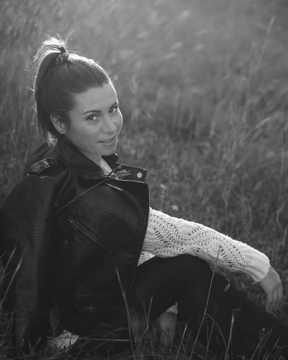Smiling brunette in leather jacker sitting in grass