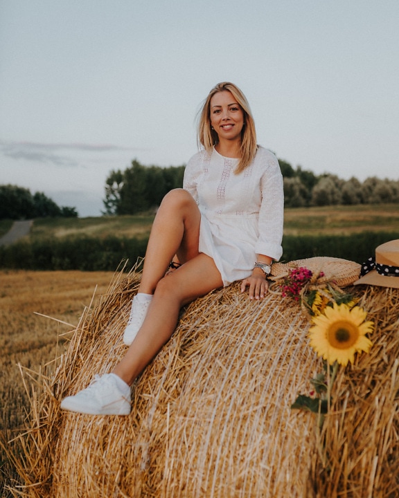 Rozkošná blondýnka se usmívá sedí na kupce sena