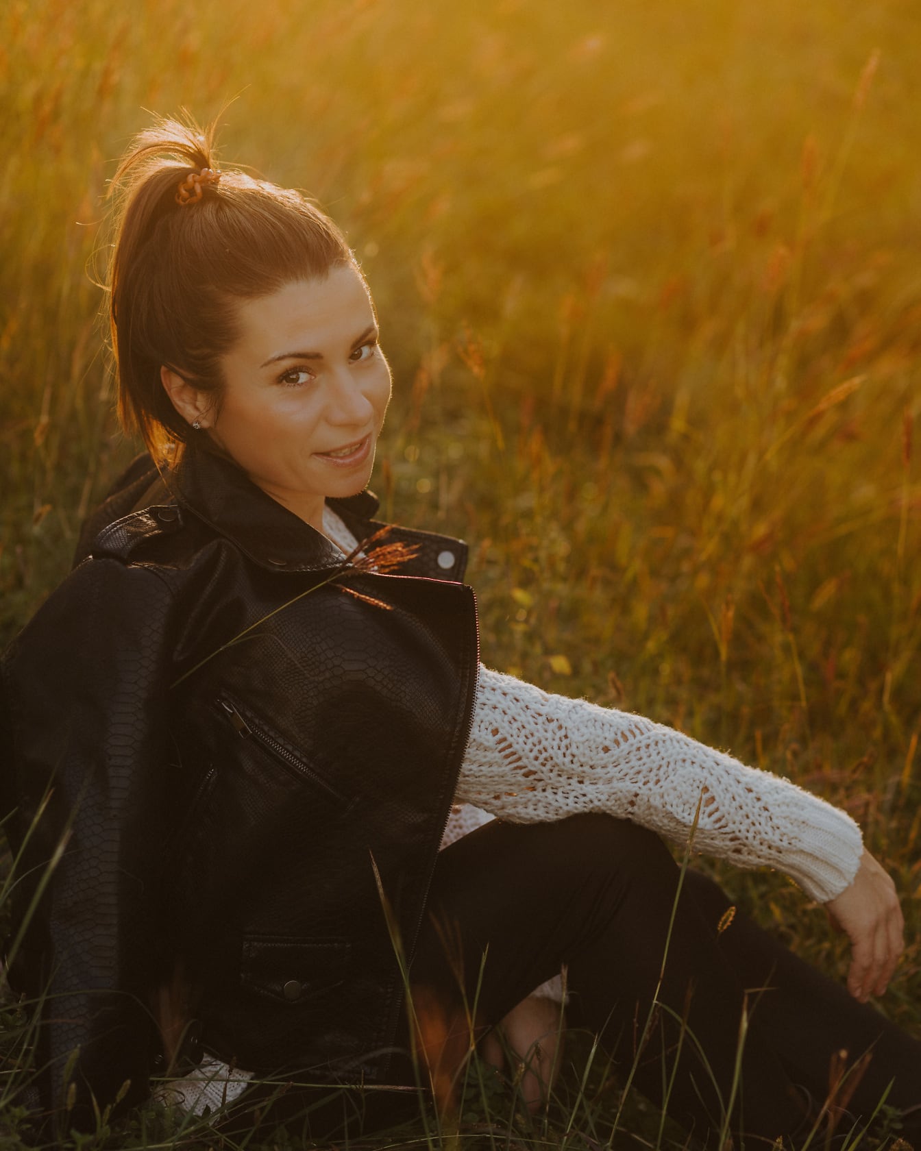 Beautiful brunette sitting in meadow with sunrays in background