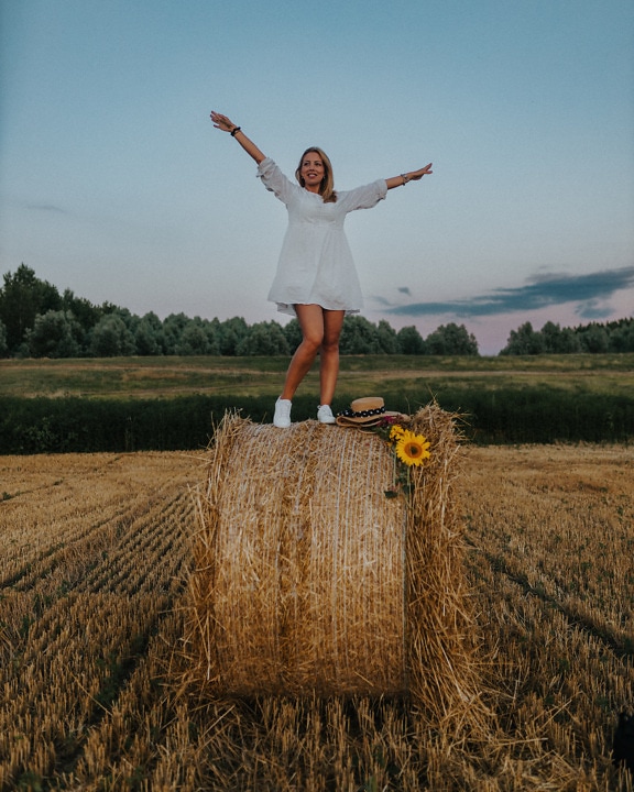 Happy blonde photo model standing on haystack