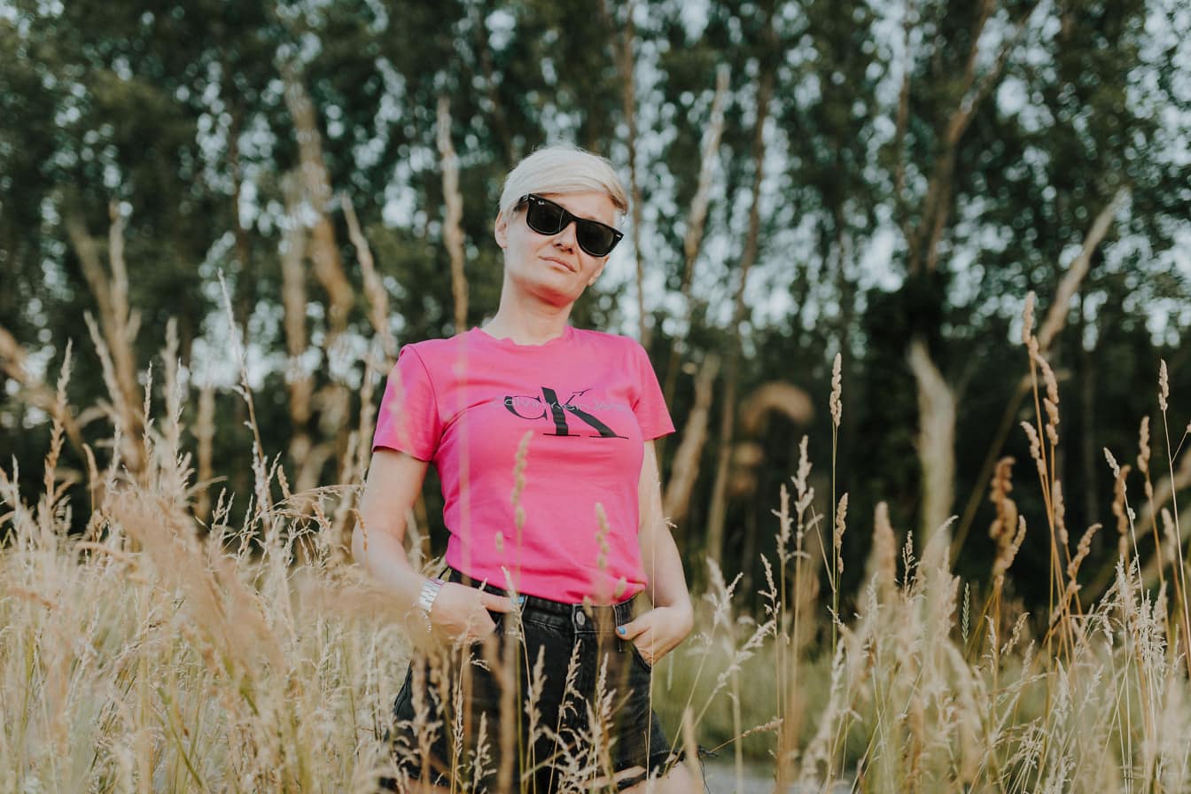 Blondínka v ružovkastej maškarnej košeli pózujúca v tráve