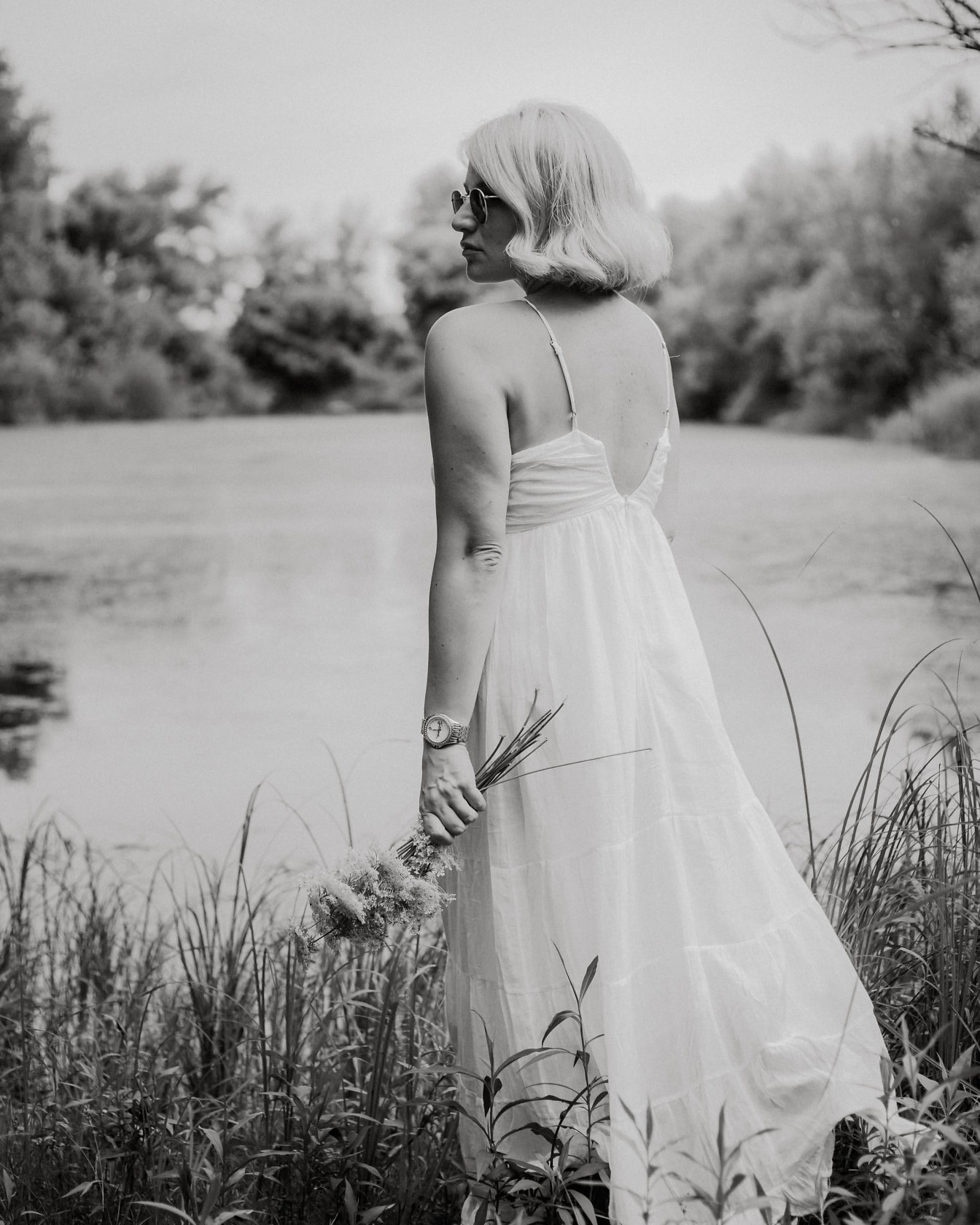 Blondine poserer i hvid kjole ved søen monokromt portræt