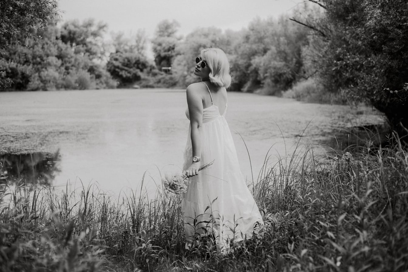 Hermosa rubia en vestido blanco por foto monocromática junto al lago