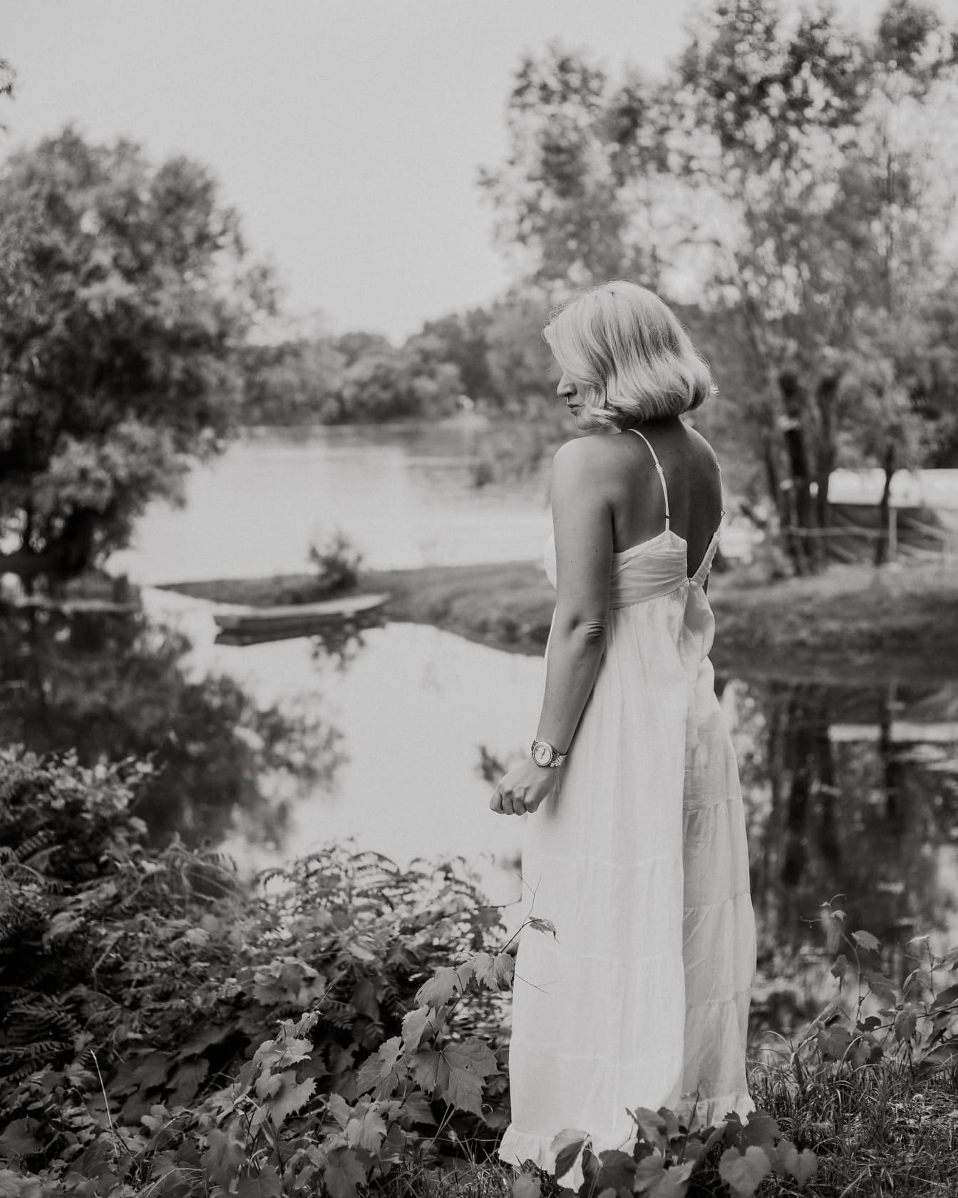 Göl kenarında siyah beyaz poz veren süslü beyaz elbiseli kadın