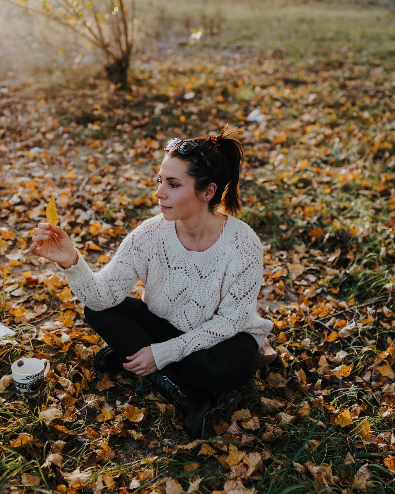 Bella giovane donna bruna che si siede sulle foglie in autunno