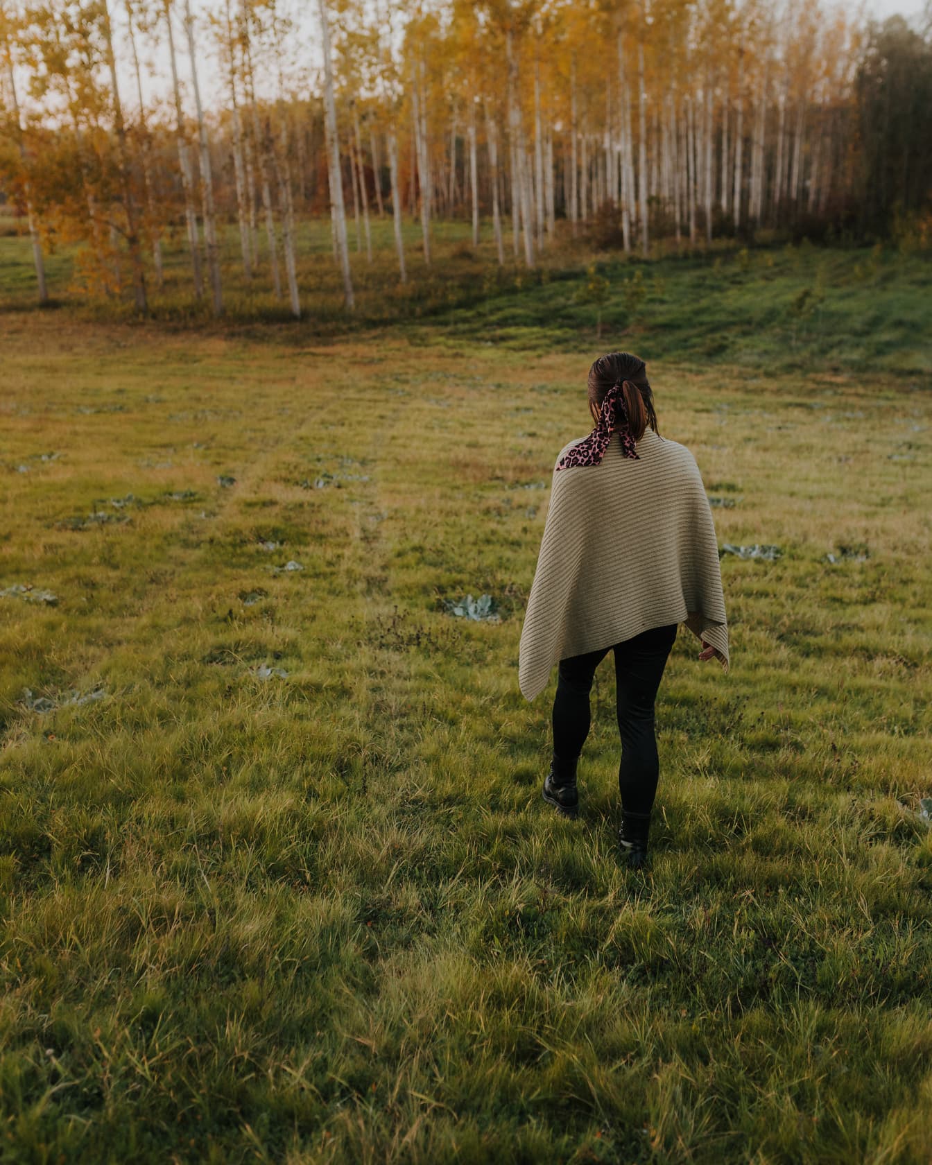 黒いズボンとセーターを着て野原を歩く女性