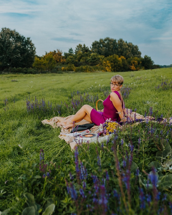 Hyvännäköinen nainen poseeraa piknikviltillä violetissa mekossa