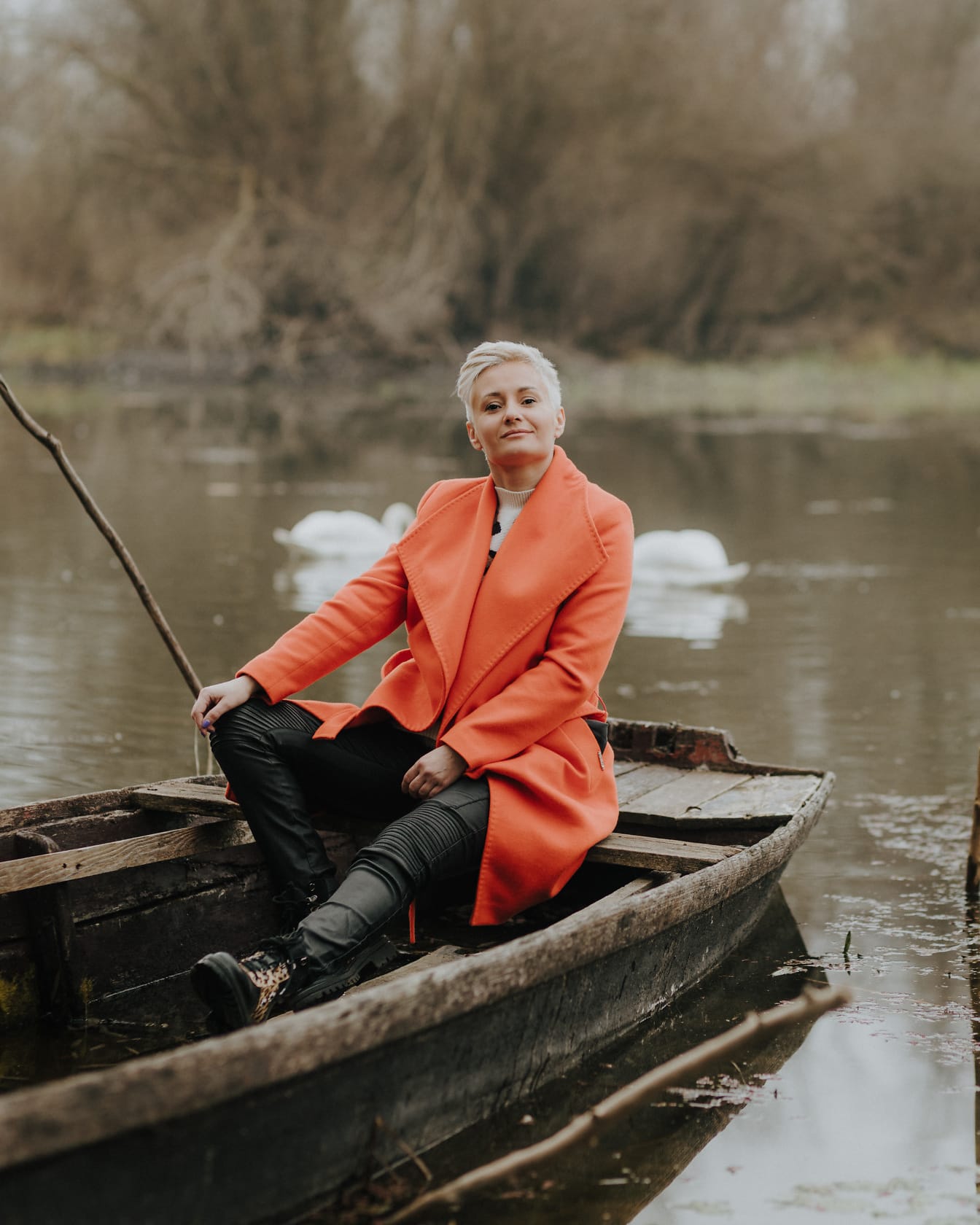 Wanita ceria dengan mantel warna oranye dan celana kulit duduk di perahu