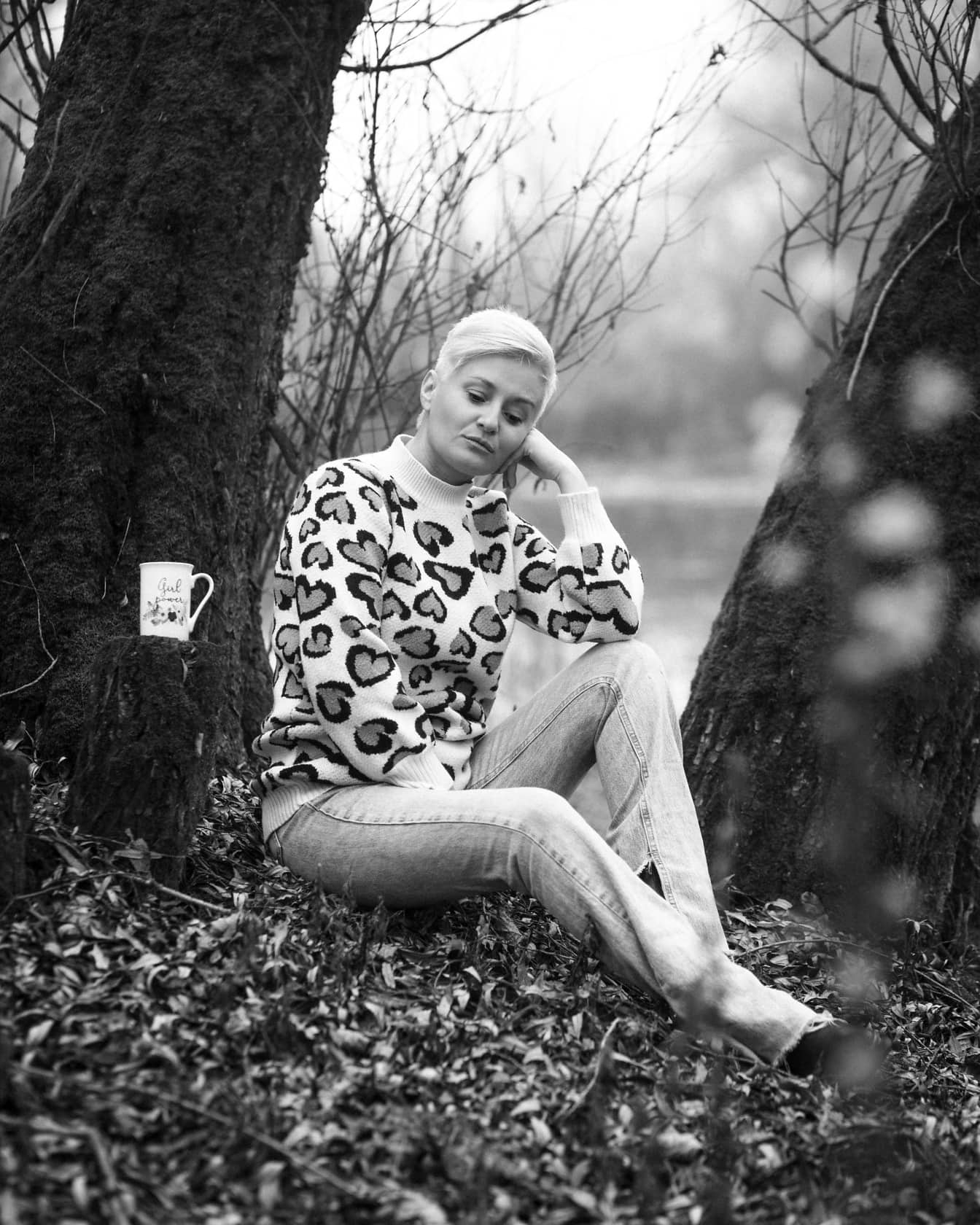 Mulher nova sentada pelo tronco da árvore e pensando foto monocromática