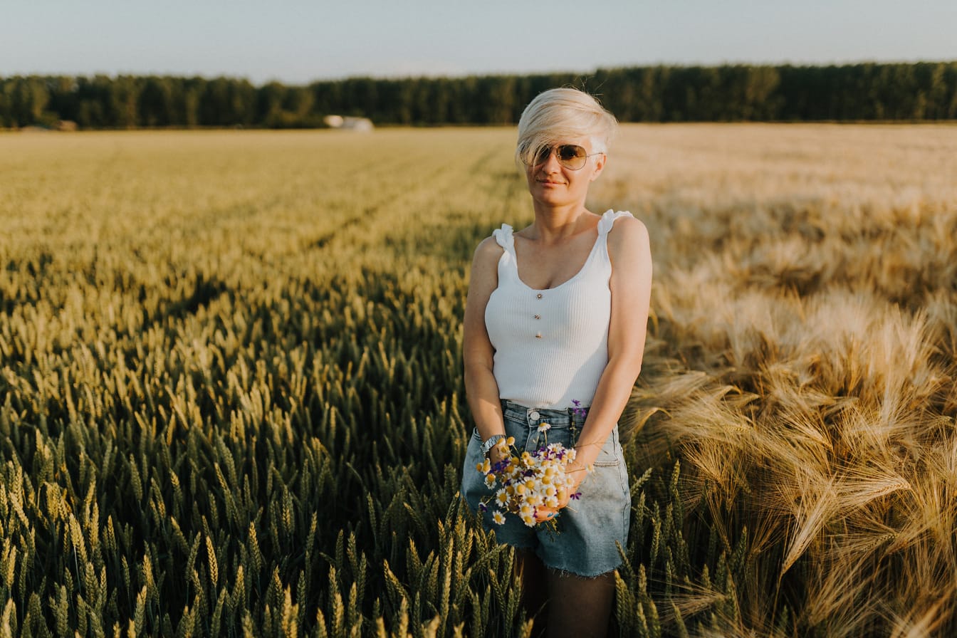 Mlada žena pozira u polju pšenice s buketom cvijeća