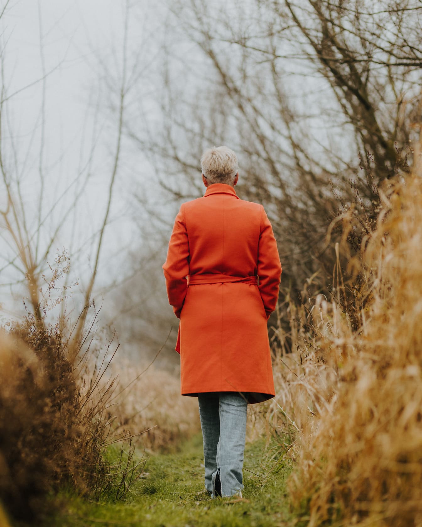 秋の田舎をオレンジイエローのコートを着て歩く女性