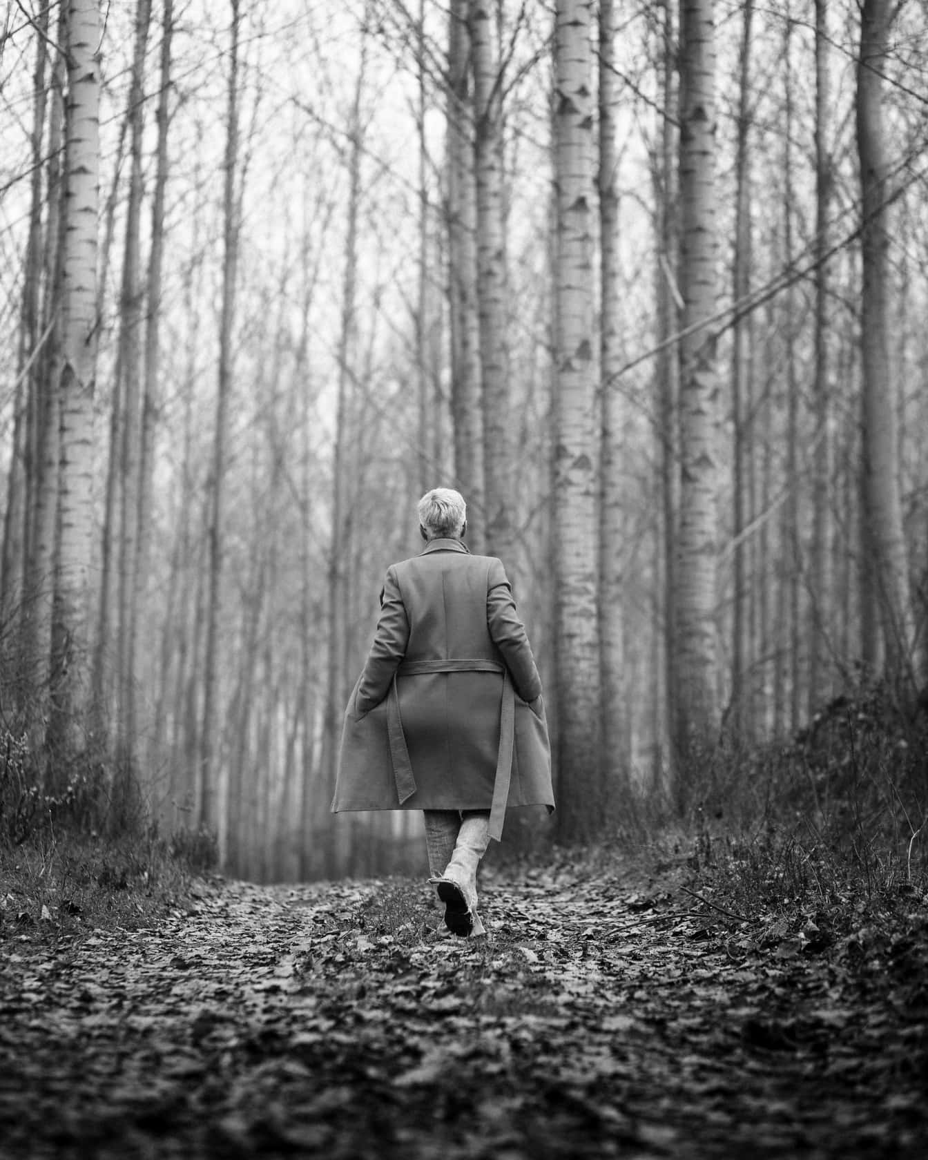 Kobieta idąca w płaszczu po leśnej drodze monochromatyczne zdjęcie