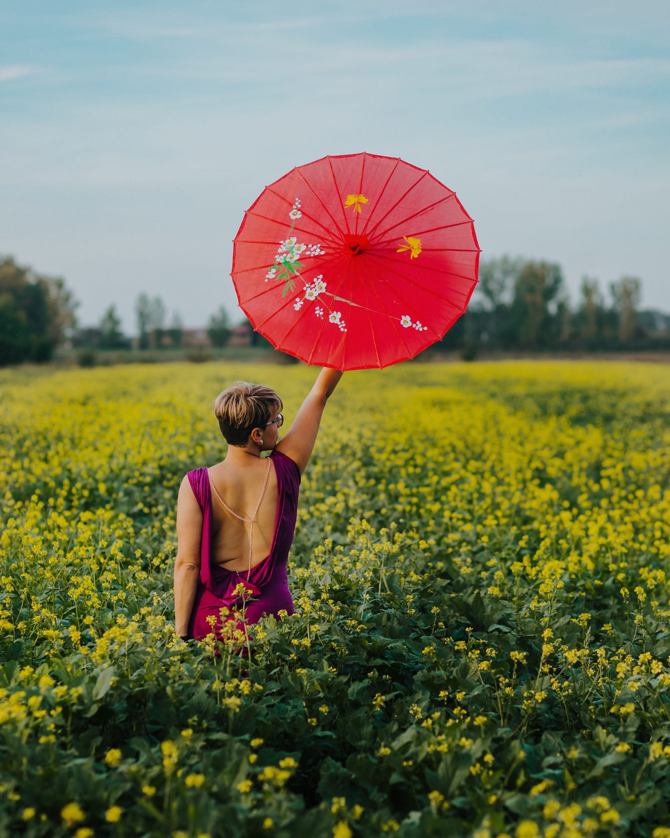 Capelli corti di bell’aspetto bionda con ombrello rosso in campagna