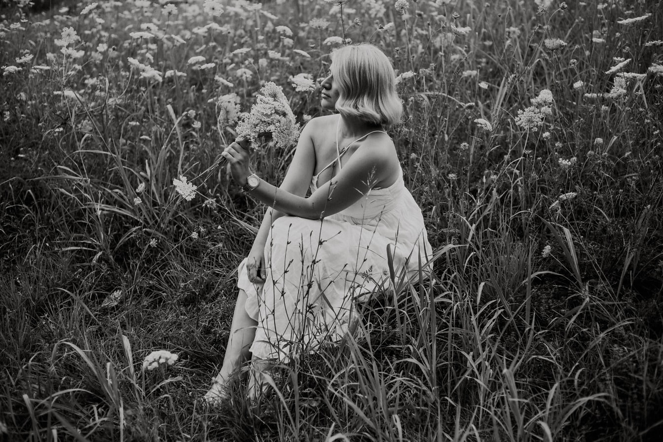 穿着白色连衣裙的好看的女人坐在草地上单色照片