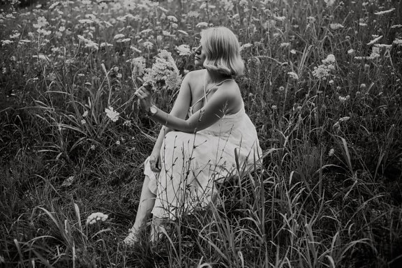 Good looking woman in white dress sitting in meadow monochrome photo