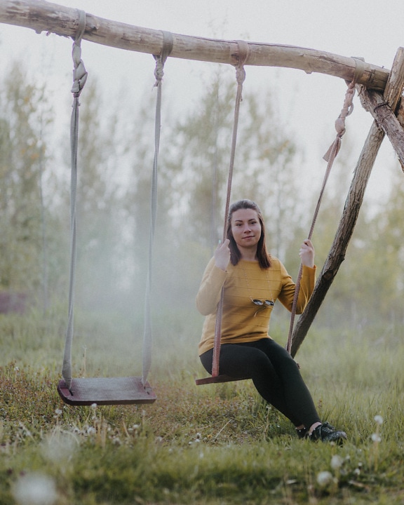 Jolie femme assise sur une vieille balançoire rustique en bois