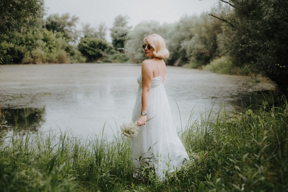 Nydelig blond brud i hvit kjole ved innsjøen