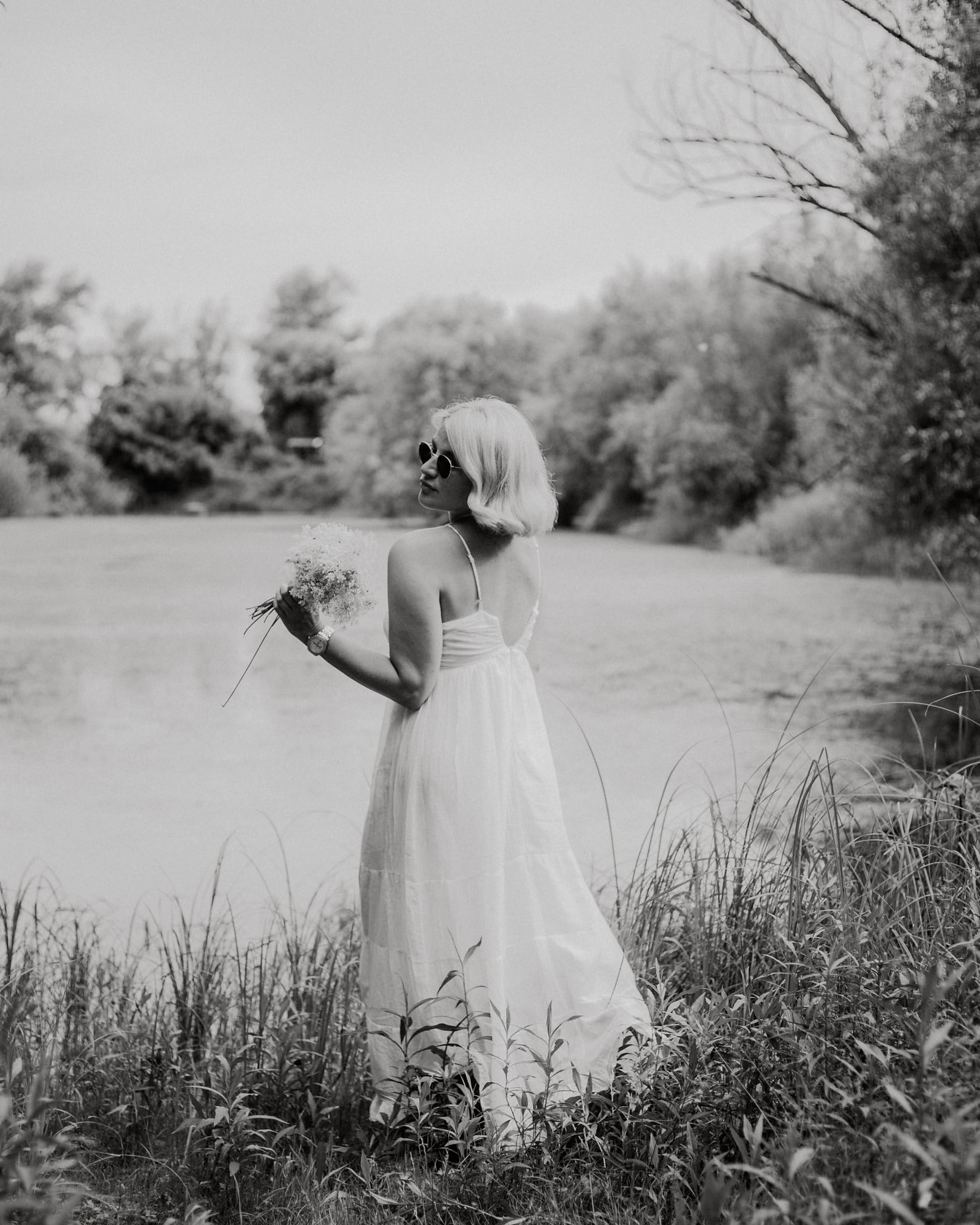 Prachtige bruid met wildflowersboeket door meer zwart-wit foto