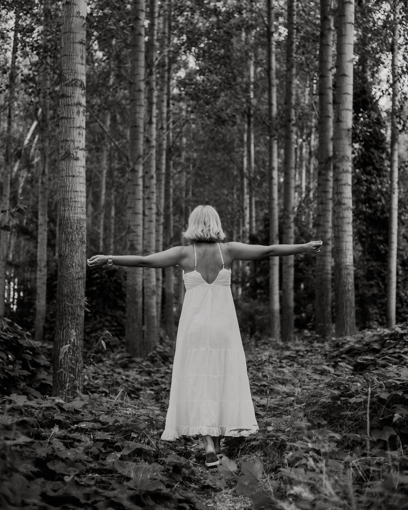 Vrolijke vrouw in witte kleding in bos zwart-wit fotografie