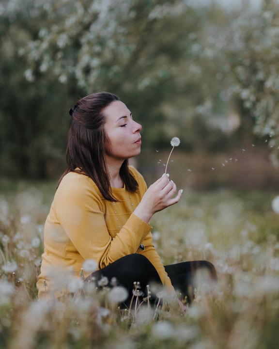 Žena na livadi i puhanje cvijeta maslačka