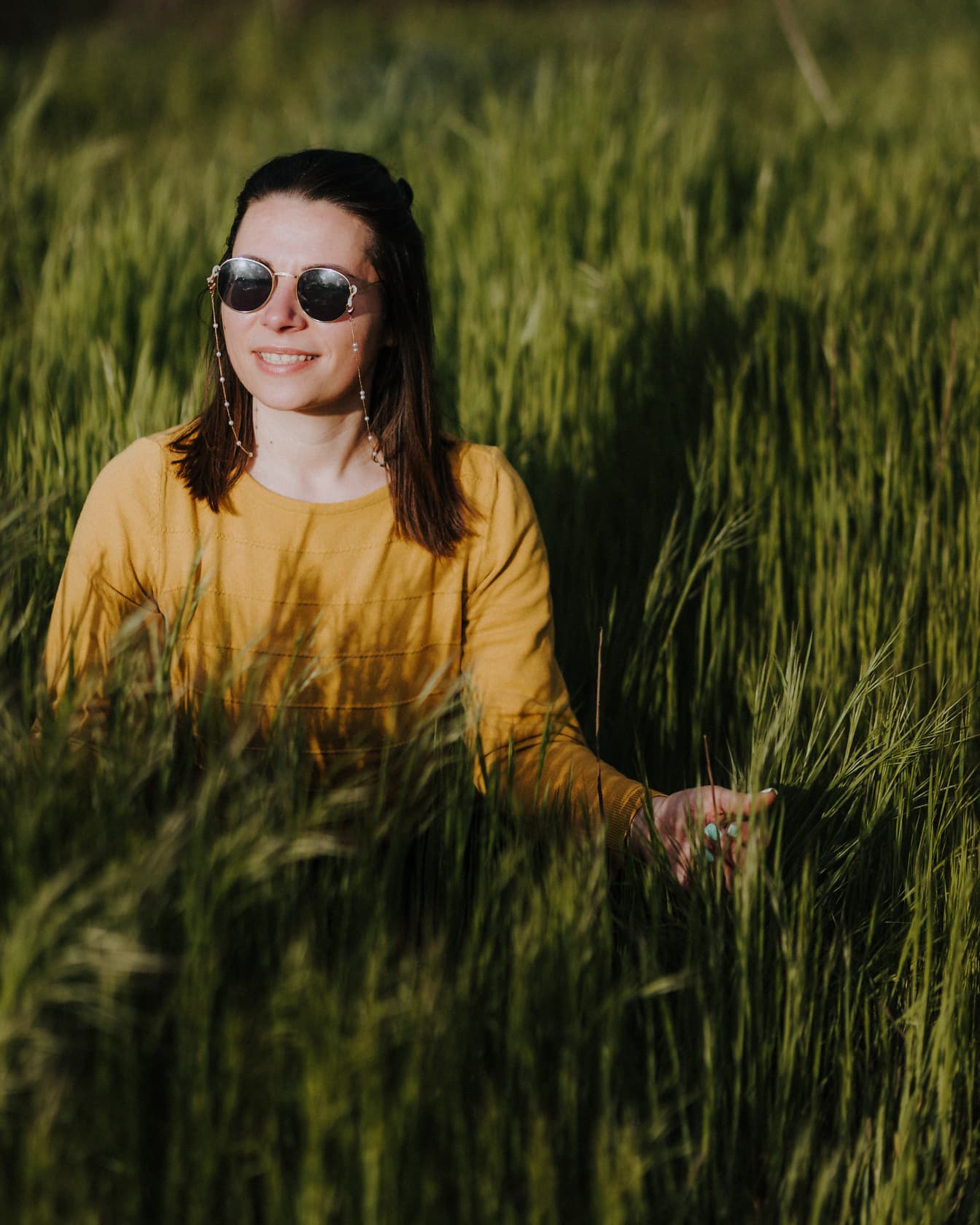 Mulher alegre sorrindo no campo de trigo verde no dia ensolarado