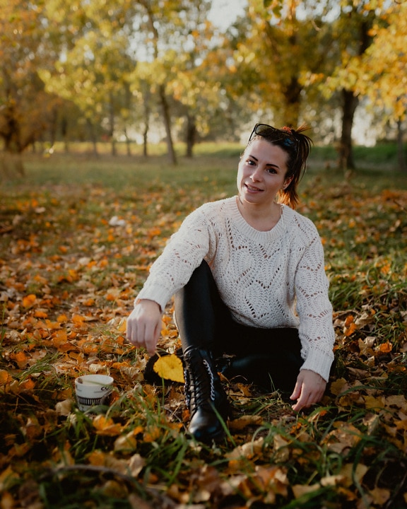 Pretty cheerful brunette sitting at ground in park at autumn season