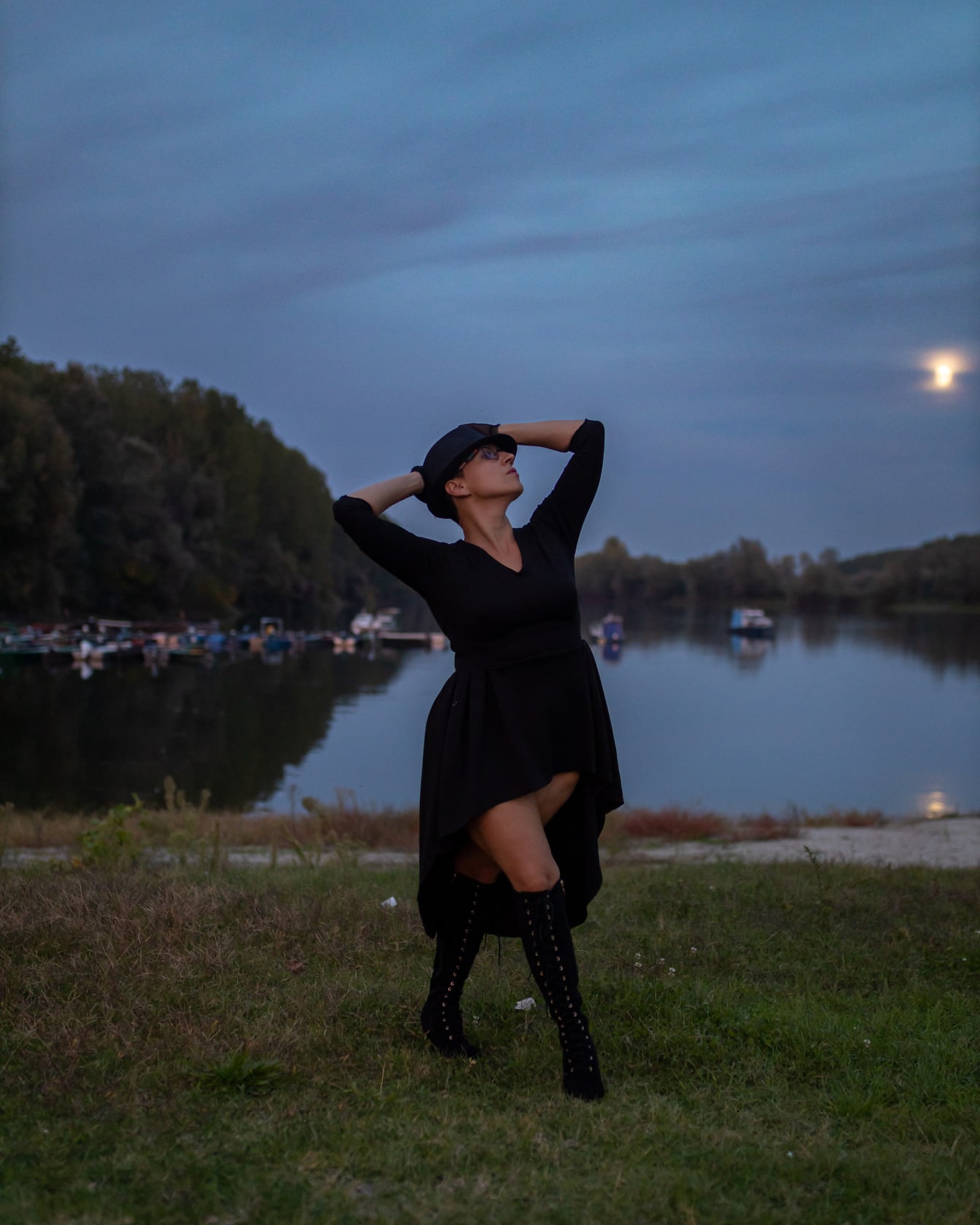 Model foto pozând în rochie neagră și cizme fanteziste
