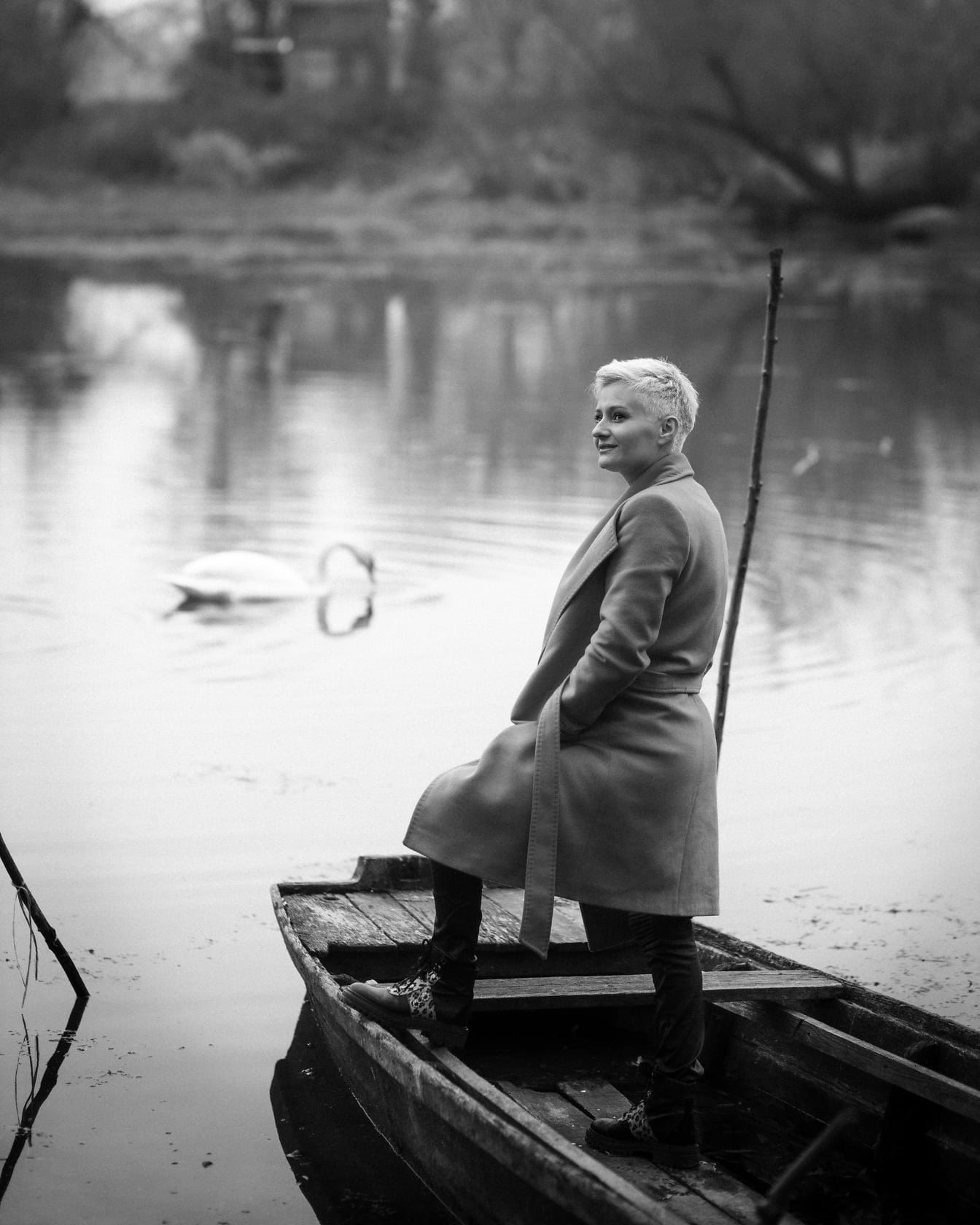 Весела млада жена в палто на брега на реката монохромна фотография