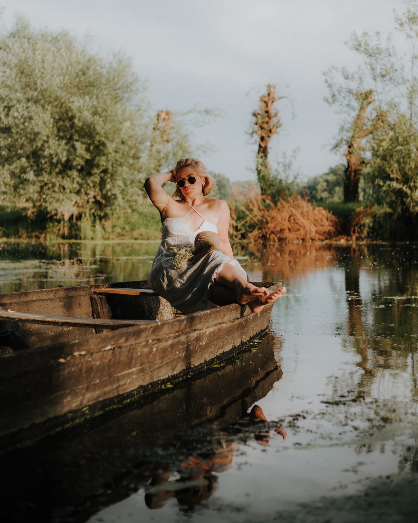 Gyönyörű hölgy ül egy fából készült csónakban a tóparton