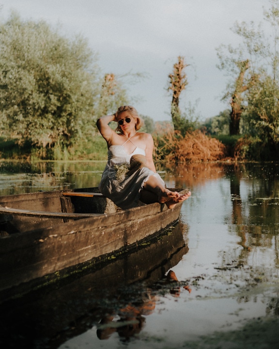 Hermosa dama sentada en un bote de madera en la orilla del lago