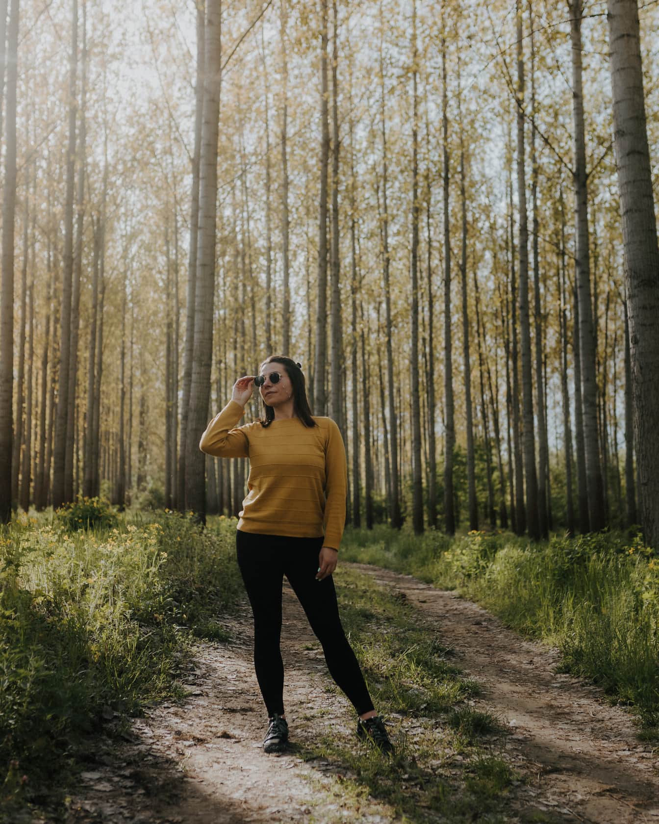 Pekná brunetka so slnečnými okuliarmi stojaca na lesnej ceste