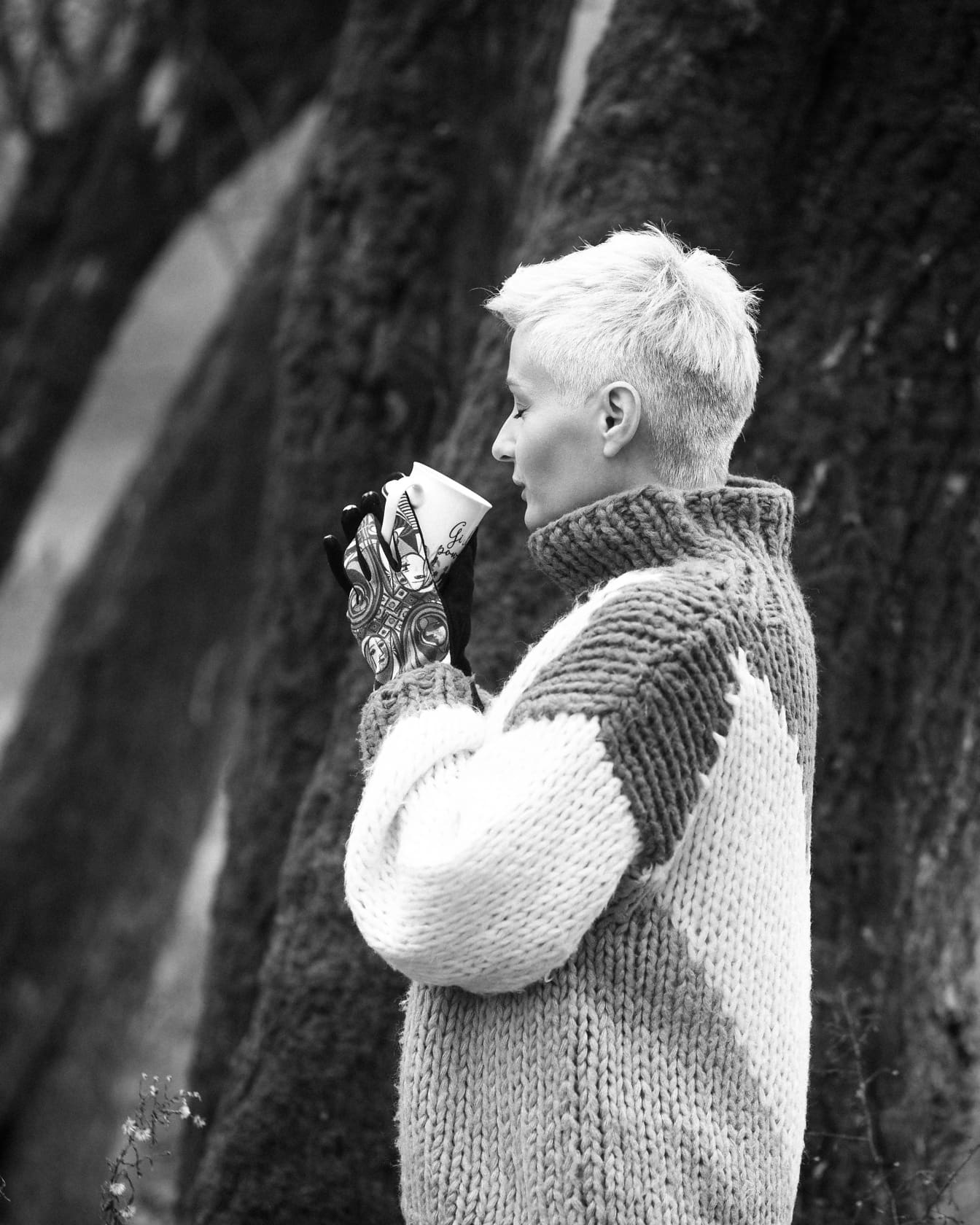 Người phụ nữ mặc áo len gỗ thủ công uống trà bên ngoài bức ảnh đơn sắc