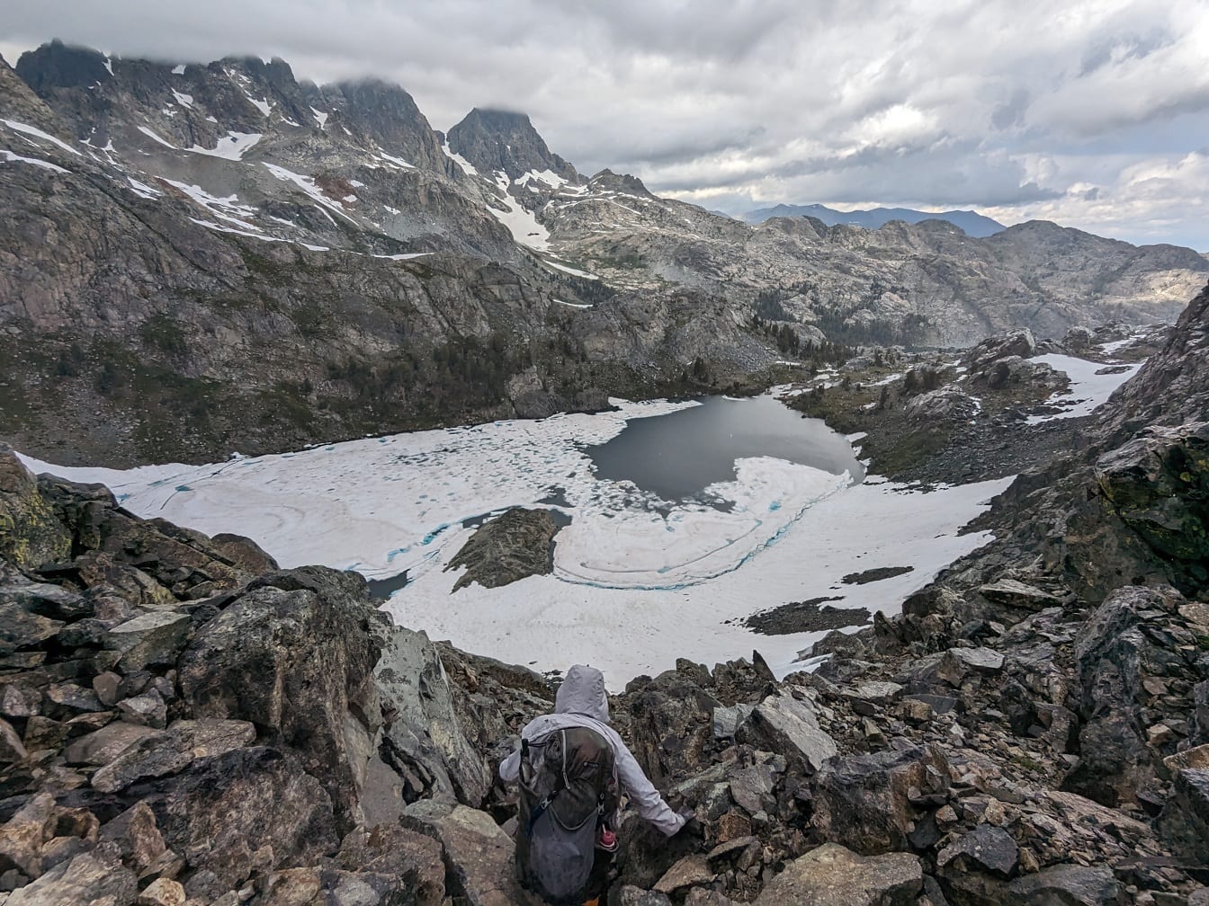 Ακραίος ορειβάτης σε βραχώδη βουνά με παγωμένη λίμνη