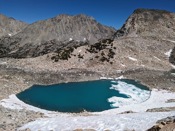Tmavě zelené zamrzlé jezero ve vysokých horách za slunečného dne