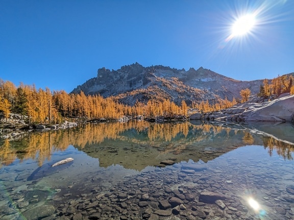 Reflecție frumoasă a apei pe malul lacului în munți, cu soare strălucitor