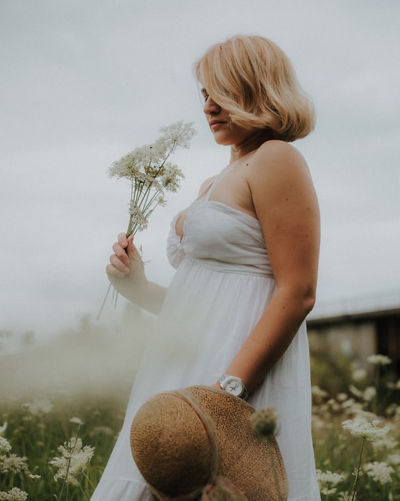 Blonde with white flower and white dress in meadow