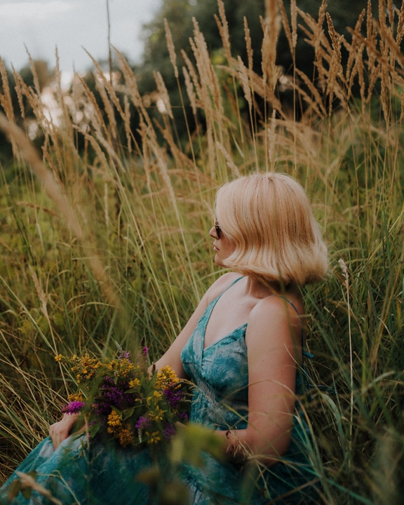 Chân dung mặt bên của cô gái tóc vàng tuyệt đẹp ngồi trên đồng cỏ