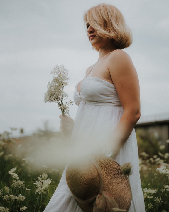 Pen blondine med hvit blomst og kjole på eng