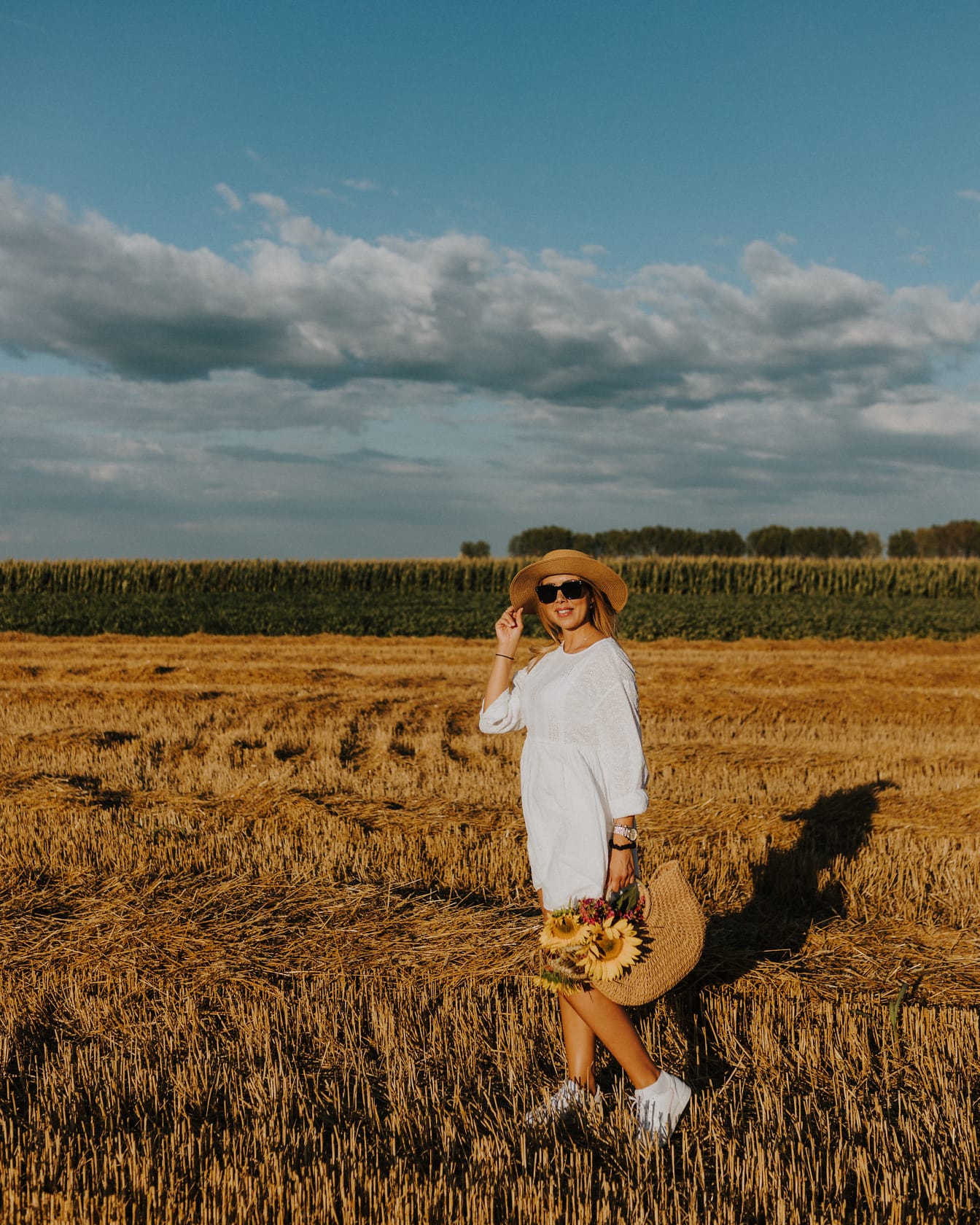 Wesoła młoda kobieta w kapeluszu na polu pszenicy latem