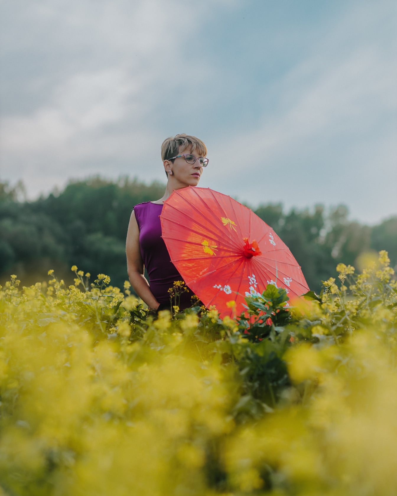 Wanita berdiri di rapeseed dengan payung merah