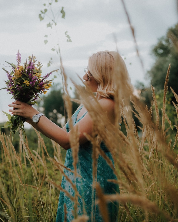 Blonde with bouquet of meadow flowers in coutryside